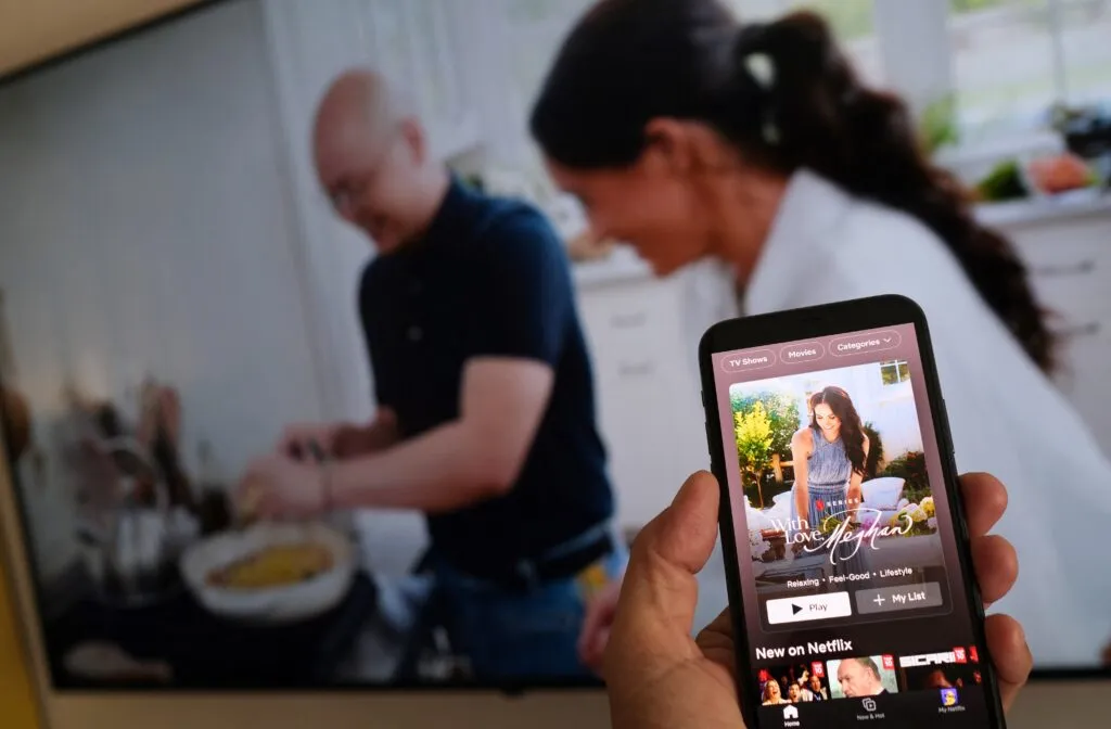 A person holds a smartphone displaying Netflix’s Meghan Markle show in front of a TV screen in Los Angeles